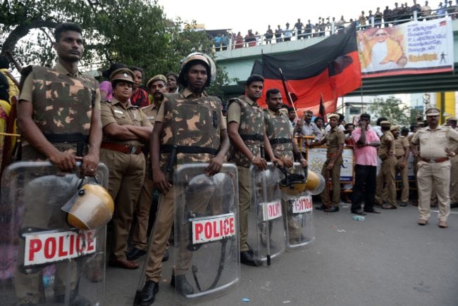 Indian policemen stand guard as supporters of the Dravida Munnetra Kazhagam party gather in front of the hospital where President M. Karunanidhi died, in Chennai on August 7, 2018. - Thousands of people desanded into mourning on August 7 in southern India after the death of revered 94-year-old political leader Muthuvel Karunanidhi. (Photo by ARUN SANKAR / AFP)        (Photo credit should read ARUN SANKAR/AFP/Getty Images)