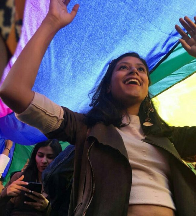 Attendee smiles with delight as they walk under a rainbow flag in the first Indian Pride parade since the decriminalisation of gay sex