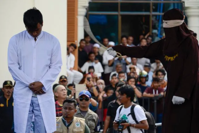 A member of Indonesia's Sharia police (R) whips a man (L) accused of having gay sex during a public caning ceremony outside a mosque in Banda Aceh