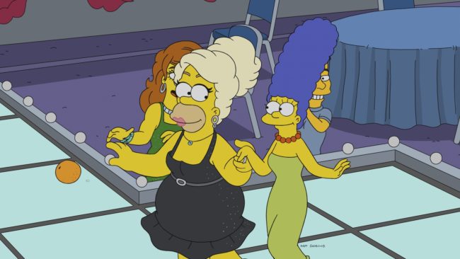Homer Simpson walks down a catwalk in drag with Marge Simpson on The Simpsons