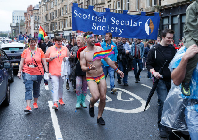 A participant wears rainbow pants and waves a flag during the Glasgow Pride.