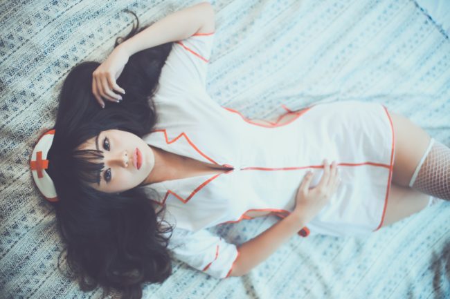 A woman lies on a bed in a nurse costume