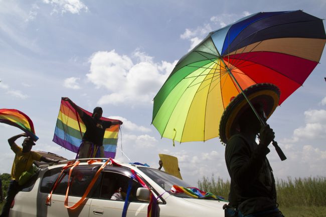 A person holds an umbrella bearing the colors of the rainbow flag as others wave flags during the the first gay pride rally since the overturning of a tough anti-homosexuality law, which authorities have appealed, in Entebbe, on August 9, 2014.