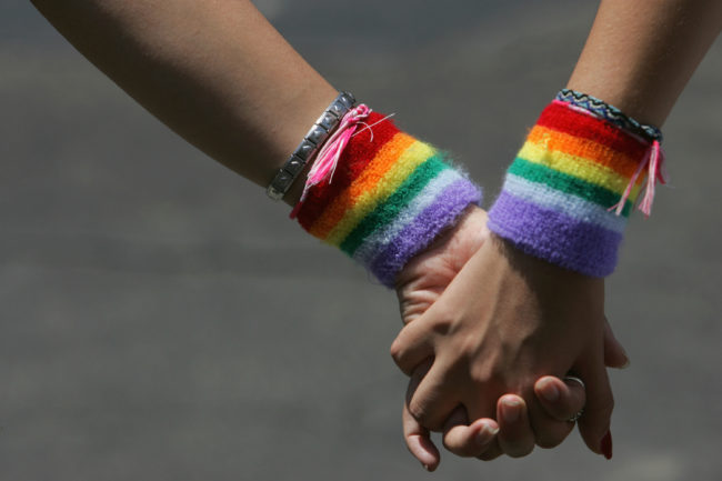 Girls holding hands with rainbow LGBT wristbands.