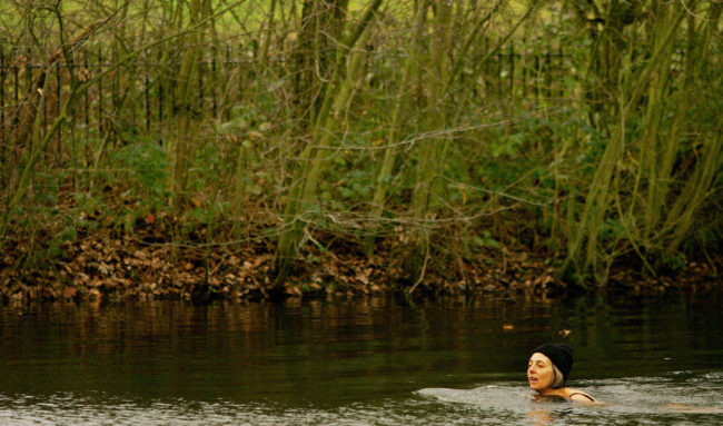 A woman swimming in Hampstead Heath wearing a cap 
