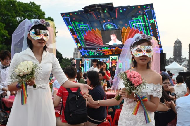 A lesbian couple wearing bridal gowns and eye masks